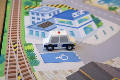 A toy police car is placed on "The Community" Town Play Mat by Habitat Mat, surrounded by imaginative play. It's parked in a disability spot and travels along vibrant roads and buildings, weaving through train tracks and green spaces for endless adventures.